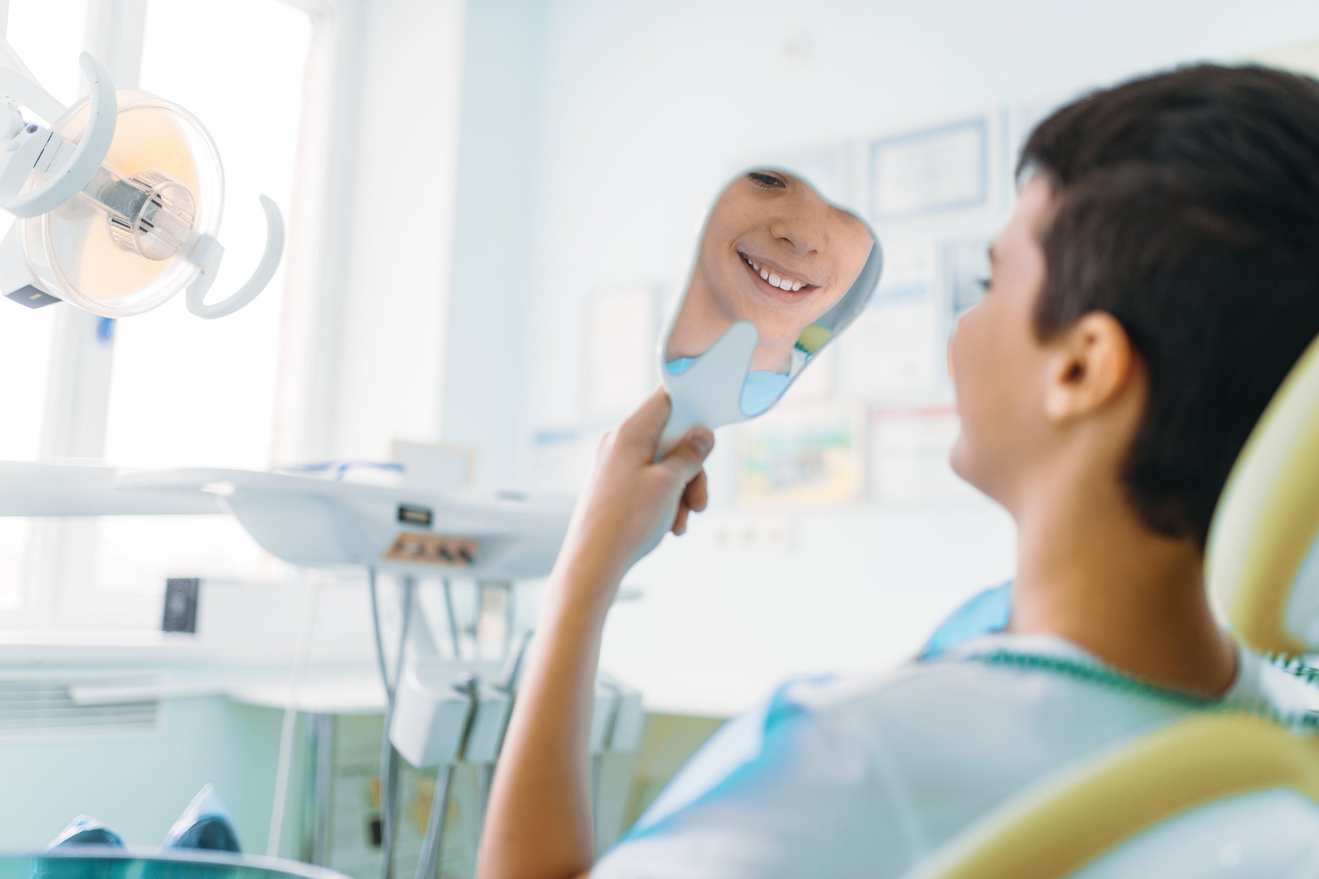 A man and child are brushing their teeth together, with the man smiling at his reflection in the mirror while holding a toothbrush.