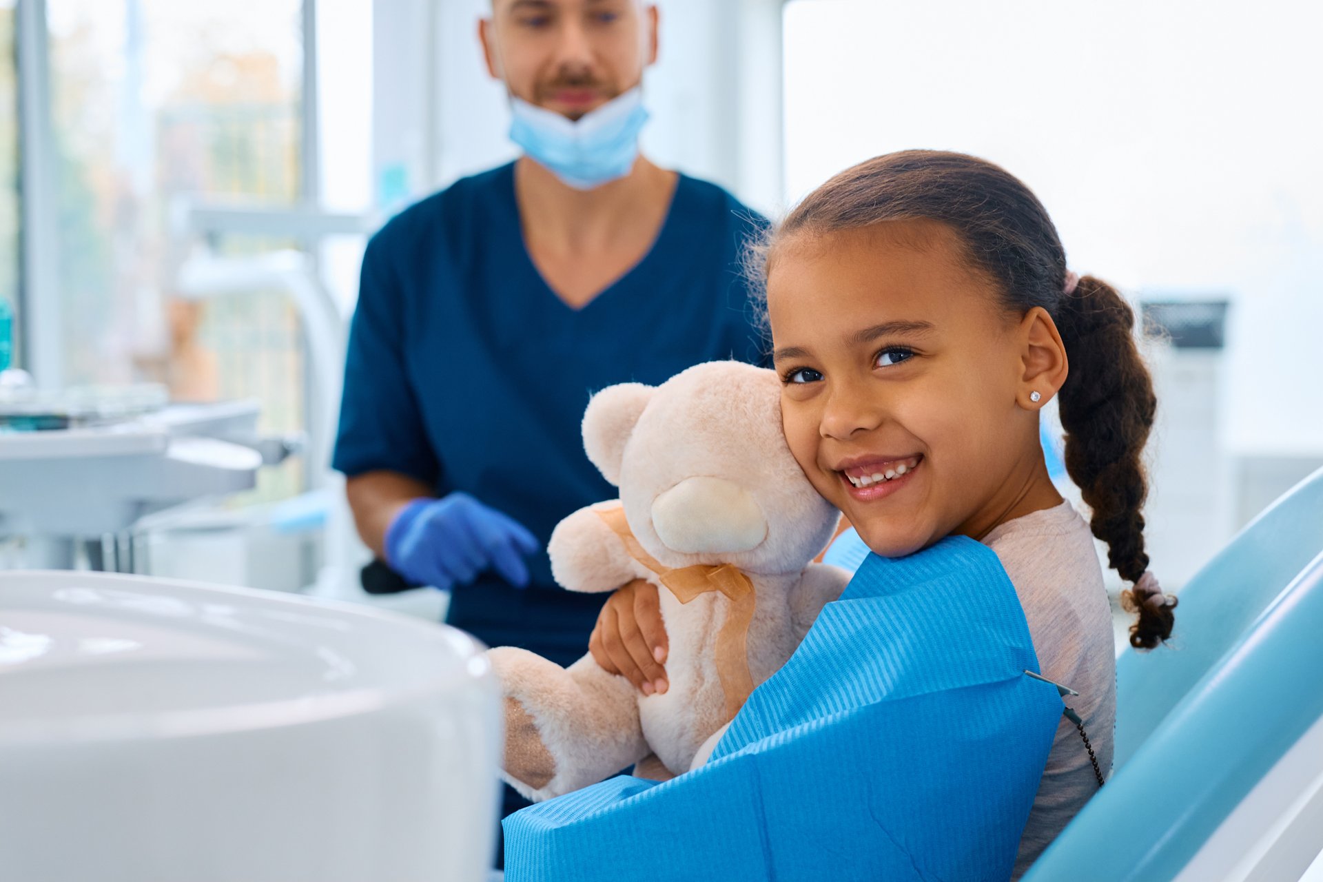 A young individual wearing a red oxygen mask while seated in a dental chair, with their mouth open for treatment.