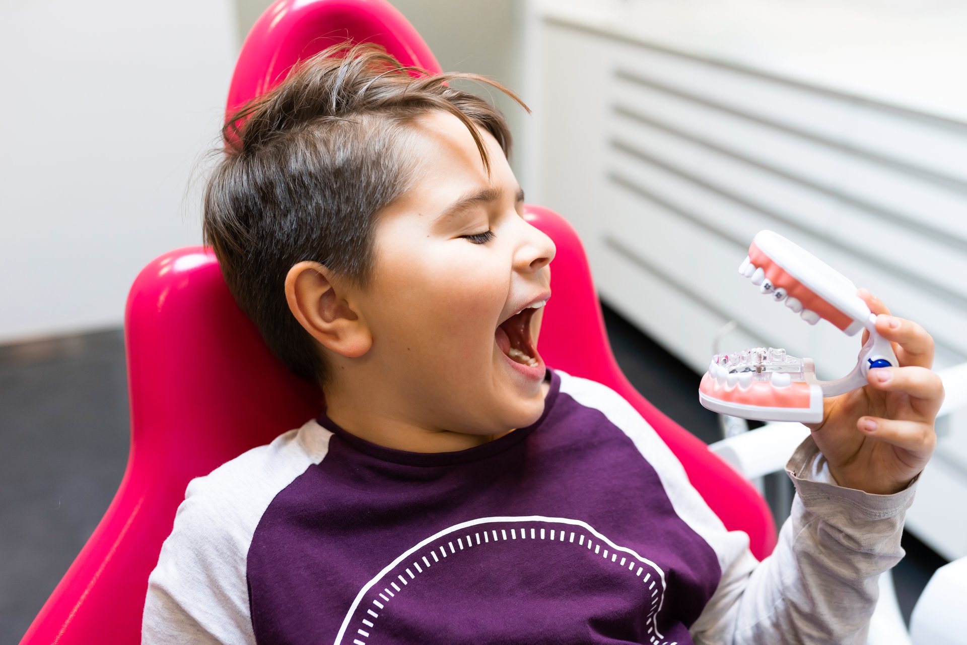 A young child giving a thumbs-up sign in front of dental chairs.