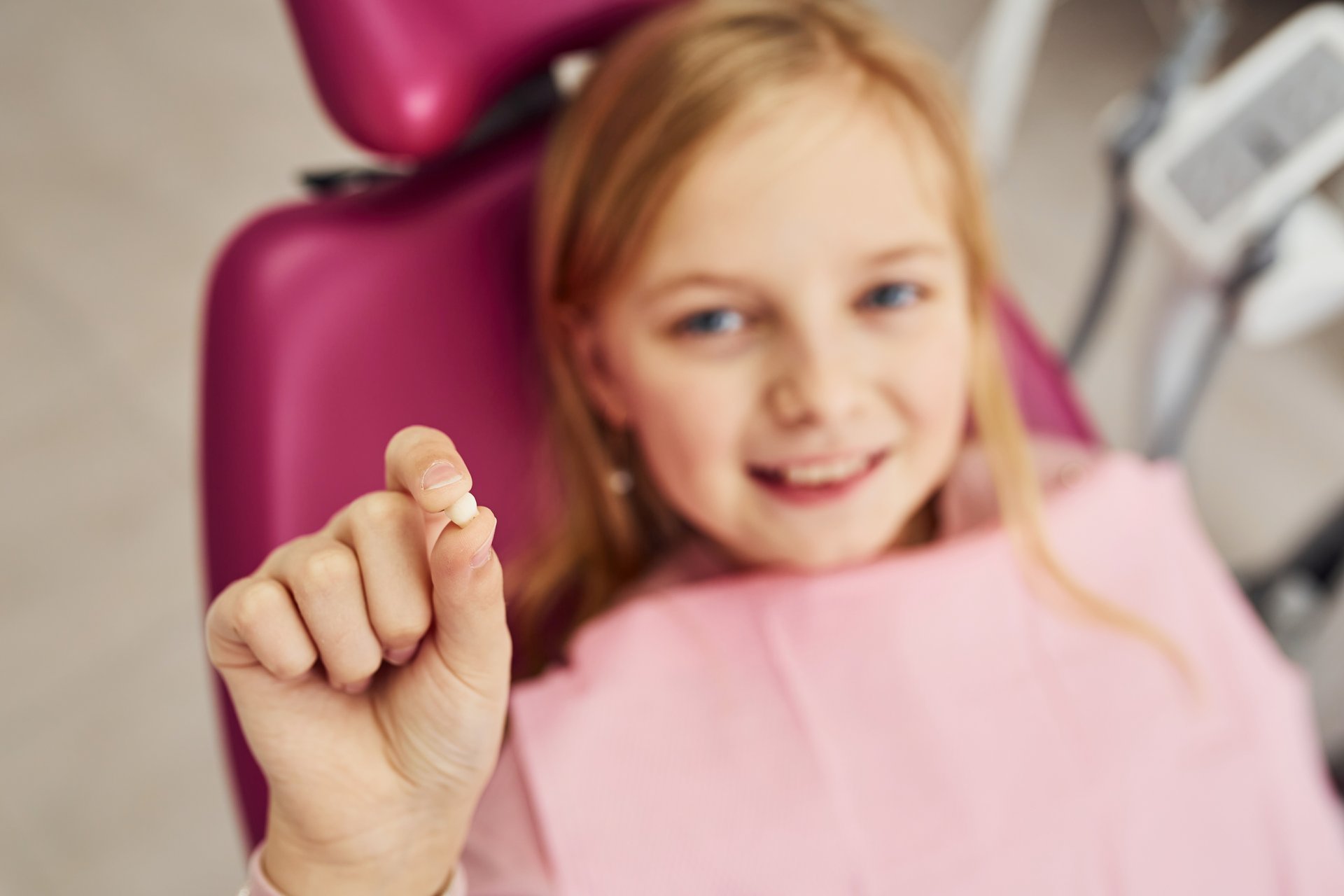 A young girl with a toothy smile holds a small white pill between her fingers, smiling broadly at the camera.